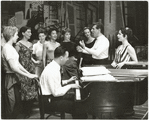 Stephen Sondheim on piano with Leonard Bernstein and Carol Lawrence (on far right) standing amongst female singers rehearsing for the stage production West Side Story.