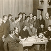 John Garfield sitting at table strumming guitar surrounded by (left to right) Kermit Bloomgarden, Robert Lewis, Aline MacMahon, Harry Carey, and Will Lee (with Philip Loeb standing in back) during rehearsals for the stage production Heavenly Express