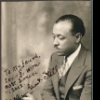 Autographed photo of William Grant Still seated in holding a pipe.
