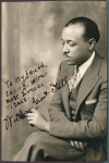 Autographed photo of William Grant Still seated in holding a pipe.
