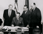 Robert C. Weaver (far right), New York State Rent Administrator, and others looking on as New York State Governor W. Averell Harriman signs documents