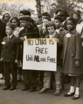 Mixed race group of children carrying sign: "No Child is Free Until ALL are Free," circa early 1960s