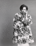 Unidentified model wearing Norman Norell flower petal opera cloak, holding left hand to side of face
