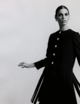 Unidentified model wearing dark Norman Norell suit, collarless jacket with rhinestone buttons and skirt with pleats
