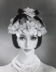 Headshot of model shoulders bear wearing flower hat and strands of crystal and glass beads