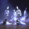Dancers wearing clown-like costumes and flowing white dresses in scene from ballet "Miracolo d'Amore".