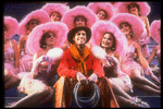 Actor Keith Carradine surrounded by beautiful dancing girls in scene fromBroadway show "The Will Rogers Follies.