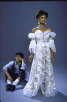 Full length shot of Vanessa Williams in costume (elaborate white ruffled dress) for role in show "One Man Band" with unidentified actor sitting in background.