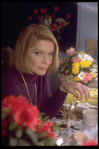 Actress Ellen Burstyn sitting at vanity table between 2 bouquets of flowers and toying with a small mirror