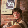Publicity photo of actor Fisher Stevens sitting in front of poster for Broadway play "Brighton Beach Memoirs" (New York)