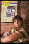 Publicity photo of actor Fisher Stevens sitting in front of poster for Broadway play "Brighton Beach Memoirs" (New York)