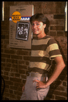 Publicity photo of actor Fisher Stevens standing in front of poster for Broadway play "Brighton Beach Memoirs" (New York)