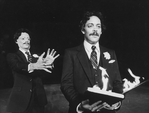 Actor Raul Julia (R) holding a book in flames as a man in a Raul Julia mask lurks behind him in a scene from the NY Shakespeare Festival Central Park production of the play "The Tempest."