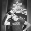 Theatrical producer Joseph Papp in "A Chorus Line" t-shirt, posing with a golden top hat in front of poster proclaiming "A Chorus Line" as Broadway's longest running show.