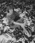 Photographer Martha Swope sitting on a floor covered with prints of her photos