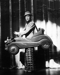 Actor Gene Nelson doing a vaudeville turn while "wearing" a tiny car in a scene from the Broadway musical "Follies.".