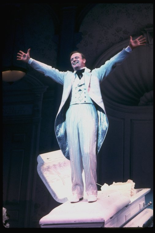 Actor Peter Allen standing atop casket in a scene fr. the Broadway musical "Legs Diamond." (New York)