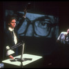 Artist Patricia Esperon speaking as portrait of Jesse Helms' eyes are projected in background in scene from play "Indecent Materials"