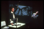 Artist Patricia Esperon speaking as portrait of Jesse Helms' eyes are projected in background in scene from play "Indecent Materials"